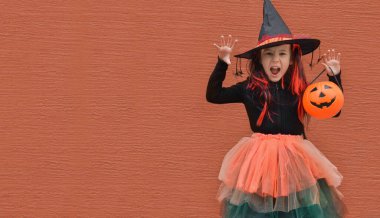 Cadılar Bayramı şeker mi şaka mı? Cadı şapkalı, turuncu duvarlı gülümseyen kız portresi. Şeker mi şaka mı? Metin için alanı kopyala