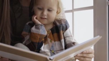Anne ve kızı Noel sabahı eğleniyorlar. Küçük kızıyla birlikte pencere kenarında kitap okuyan genç bir anne..