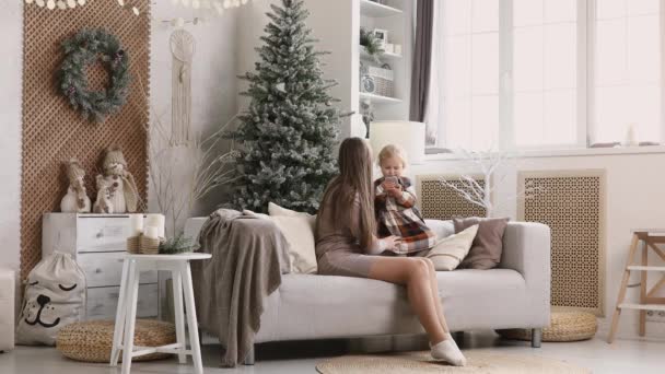 妈妈和女儿打电话 通过视频交流 在圣诞节早上用智能手机 年轻的妈妈和她的小女儿在圣诞树旁接受亲戚们的问候 — 图库视频影像