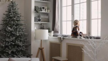 Sevimli küçük kız Noel sabahı eğleniyor. Değerli aile anı, genç kız pencereden dışarı bakar..