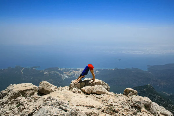 Yoga yapan kadın dağın tepesinde gökyüzüne ve denize karşı güneş selamı veriyor.