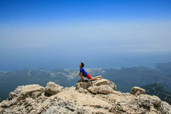 Yoga yapan kadın dağın tepesinde gökyüzüne ve denize karşı güneş selamı veriyor.