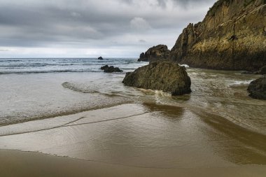 Asturias 'taki Playa del Aguilar' ın alçak gelgit ve bulutlu gökyüzü manzarası.