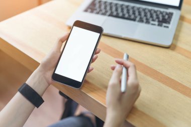 akıllı telefon tutarak ve montaj grafikleri görüntülemek için tablo ile ağaçlar ve doğa arka plan, windows üzerinde oda ofis dizüstü bilgisayar kullanarak bir kadın. Senin ekran reklam koymak için almak.