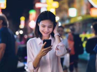 Gece şehir alışveriş caddesi ve insanlar yürüyüş bir smartphone tutan kadın portre. İletişim kavramı için teknoloji.