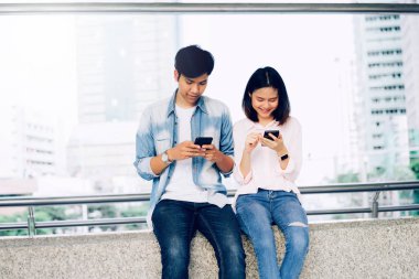 Asya genç insan smartphone kullanarak ve serbest zaman üzerinde otururken gülümseyerek. teknoloji kavramı