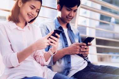 Gençlerin smartphone kullanarak ve serbest zaman üzerinde otururken gülümseyerek. teknoloji kavramı