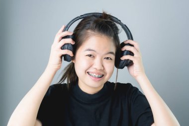 Asyalı kız siyah casual elbise siyah kulaklık müzik. Rahat ve iyi bir ruh halinde gri bir arka plan üzerinde yumuşak bir ışık verir..
