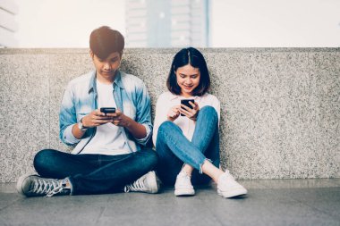 Asya genç insan smartphone kullanarak ve serbest zaman üzerinde otururken gülümseyerek. teknoloji kavramı