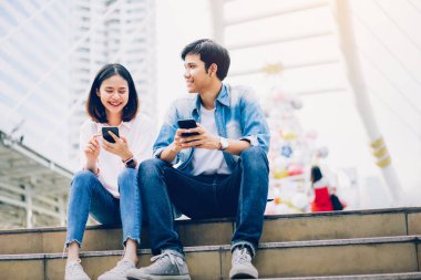 Gençlerin smartphone kullanarak ve serbest zaman üzerinde otururken gülümseyerek. teknoloji kavramı