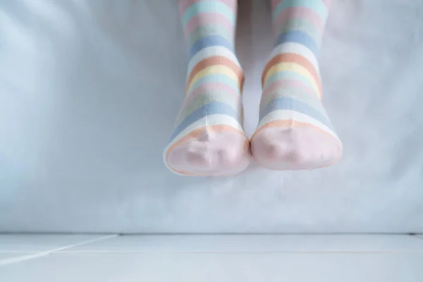 Women\'s legs in socks colors alternating, side stand on white fabric floor.