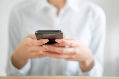 Ahşap masa üzerinde akıllı telefon kullanarak ve arkadaşlarına mesaj yazarak ellerin yakın çekim.