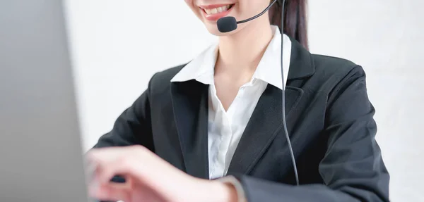 Smiling Asian woman consultant wearing microphone headset of customer support phone operator at workplace.