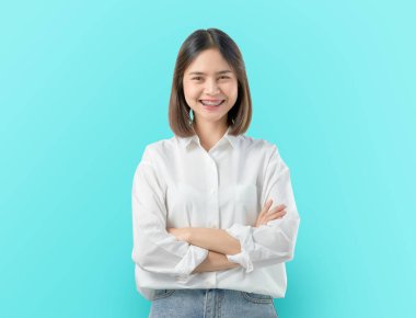 Neşeli güzel Asyalı kadın standı ve mavi arka plan üzerinde kolları geçti.