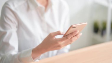 Ahşap masa üzerinde akıllı telefon kullanarak ve arkadaşlarına mesaj yazarak ellerin yakın çekim.