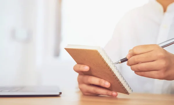 Close-up of hands holding pen and writing on notepad, paper on desk.