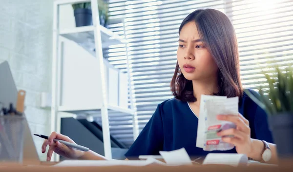 Sad Asian woman hand holding expense bill and calculation about debt bills monthly at the table in home office.