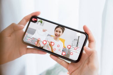 Genç Asyalı kadınlar evdeki müşterilere sosyal medyada akıllı telefonla kıyafetlerini ve satışlarını gösteriyor. Ağ teknolojisi kavramı.