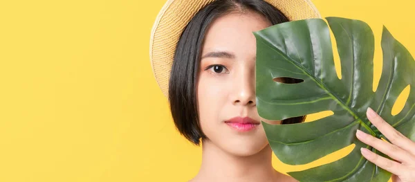 緑色の葉を持つアジアの女性の美しさのショットは オレンジの背景に顔に触れる — ストック写真