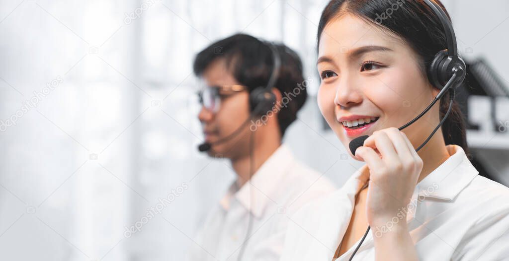 Smiling Asian businesswoman consultant wearing microphone headset of customer support phone operator at workplace.