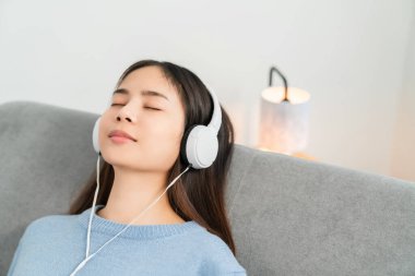 Mutlu gülümseyen Asyalı kadın tatilde beyaz kulaklıklardan müzik dinliyor..