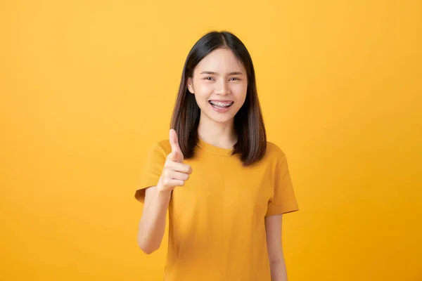 Genç Gülümseyen Asyalı Kadın Sarı Arka Planda Durup Parmak Işareti — Stok fotoğraf