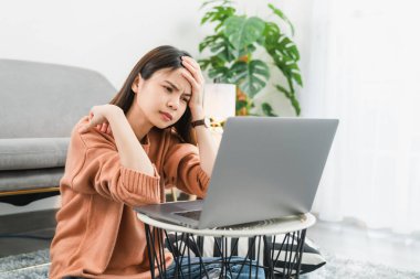 Yorgun genç Asyalı kadının başı ağrıyor çünkü dizüstü bilgisayar kullanıyor ve uzun süre evde çalışıyor..