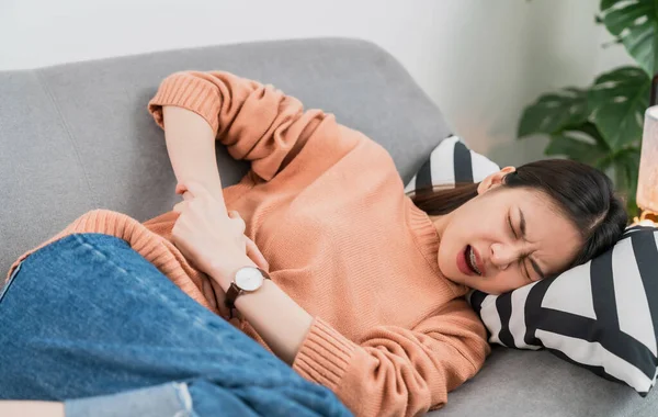 Young Asian woman hands holding the stomach on sofa and pain period cramps because having menstruation.