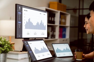 Dizüstü bilgisayarlar üzerinde çalışan iş adamları masadaki bilgisayar ekranları ve tabletlerle istatistik grafiklerini gösteriyorlar.