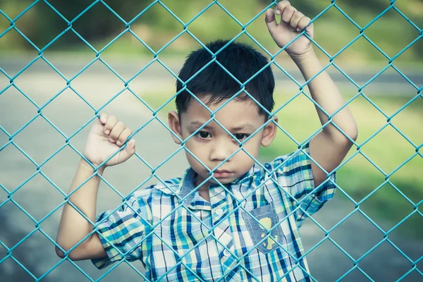 Çocuğun duygusal ifade ile çitin arkasında duruyor.