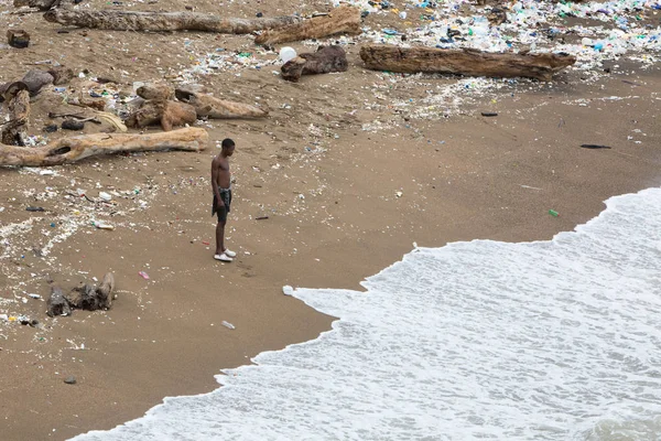 Dominik Cumhuriyeti, Santo Domingo - 7 Eylül 2017: Siyah adam deniz kıyısında plastik ve çeşitli çöp yığını içinde kıyıda duruyor. İnsan çevreyi kirleter. Saf gezegen