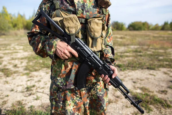 Soldier holds a machine gun in hands, close-up. Man in green camouflage on the battlefield with a black assault rifle