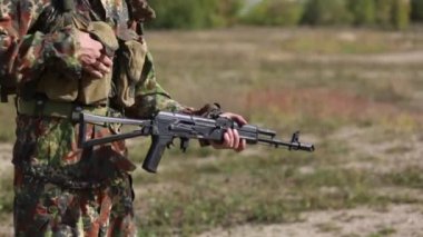 Kamuflajlı bir adam ateş etmek için silah hazırlıyor. Popoyu açar, bir dergiyi Kalaşnikof tüfeğine kurşun yağdırıp deklanşörü defore eder. Ak47 yükleme Yakın çekim. Asker el şarj makineli tüfek