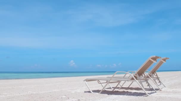 ターコイズブルーの水を持つ熱帯の白い砂浜の2つのサンラウンジャー 背景にココナッツの木 スローモーションカメラ 海沿いのホテルでの休暇と美しい日焼け — ストック動画