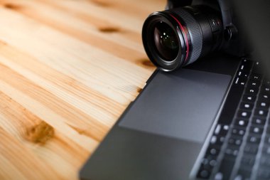 Metin tasarımı için fotokopi alanı olan ahşap masa arkaplanındaki fotoğrafçı işyeri. Modern laptop ve dijital kamera lensi. Minimalizm üst görünümü