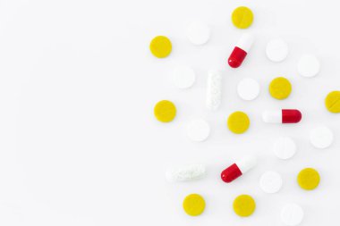 Renkli hapların üst görüntüsü beyaz bir masaya saçılmış. Hastaya yazılan beyaz, sarı ve kırmızı ilaç kapsülleri. İzole edilmiş ilaç kopyalama alanı minimalist arkaplan