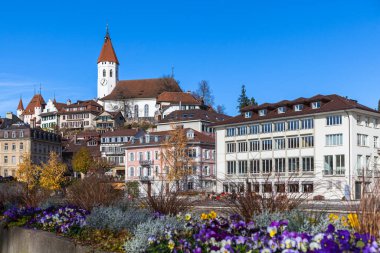 Güneşli bir sonbahar gününde Aare nehri kıyısındaki Thun kasabasının güzel manzarası. Arka planda Thun Kalesi ve mavi gökyüzü. Önde çiçekler, Bern Kantonu, İsviçre..