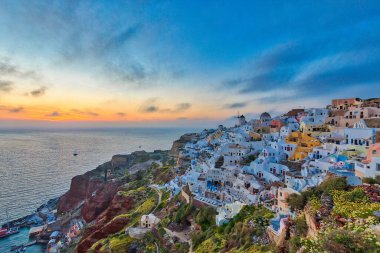 Alacakaranlıkta Santorini adasındaki Oia köyünün göz kamaştırıcı manzarası, renkli alacakaranlık ve beyaz evler, yel değirmeni, Yunanistan.