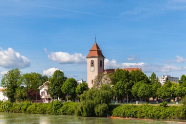 Güneşli bir günde Ren nehrinde saat kulesi olan küçük bir kilisenin huzurlu manzarası, Almanya ile İsviçre arasındaki Basel sınırında..