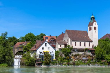 Güneşli bir günde Ren nehrinin kıyısındaki küçük bir kilisenin huzurlu manzarası, Almanya ile İsviçre arasındaki Basel sınırında..