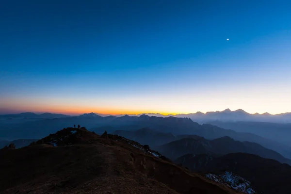 Panorama view of the twilight and moon in the sky with silhouette of mountains and cloudscape on top of Cattle Back Mountain (Niubeishan) in Sichuan Province, China
