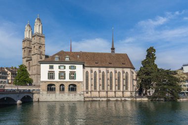 Grossmuenster (Grossmunster) kilisesi ve Wasserkirche (Su Kilisesi) güneşli bir yaz gününde Zürih, İsviçre 'de Limmat nehrinin karşı kıyısından güneşli bir manzaraya sahiptir.