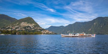 Lugano Gölü manzarası, Lugano şehri, Monte Bre dağı ve İsviçre Alpleri güneşli bir yaz gününde mavi gökyüzü bulutu, ön planda seyahat gemisi, İsviçre Ticino Kantonu