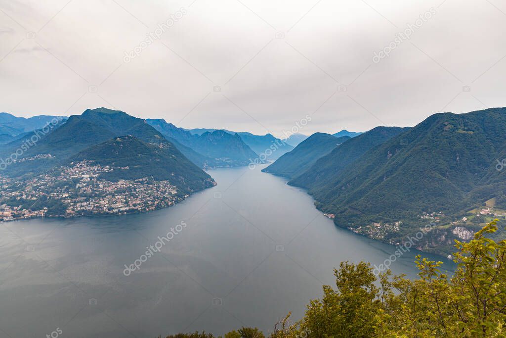 Aerial panorama view of Lugano Lake, cityscape of Lugano, mountain Monte Bre and Swiss Alps on a cloudy summer day from top of Monte San Salvatore, Canton of Ticino, Switzerland