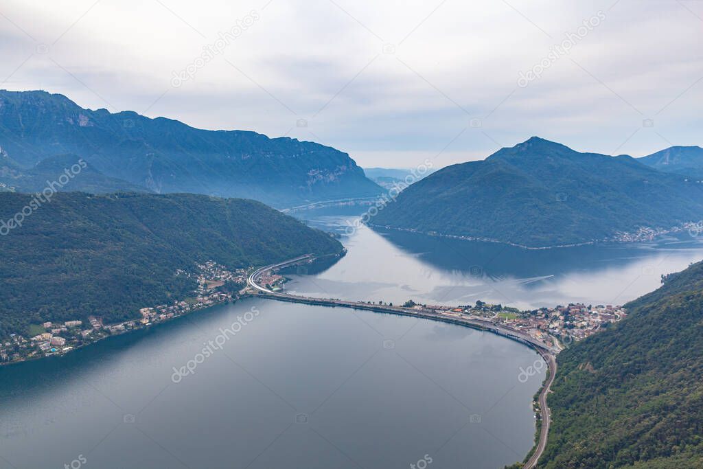 Aerial panorama view of Lugano Lake towards Melide causeway with Swiss Alps mountain Monte San Giorgio on a cloudy summer day from top of Monte San Salvatore, Canton of Ticino, Switzerland