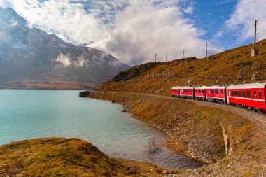 Rhaetian demiryolu kırmızı treninin güzel manzarası sonbaharda Lago Bianco göl tarafında mavi gökyüzü bulutuyla ilerliyor, demiryolu hattı Bernina Express, Grisonlar Kanonu, İsviçre