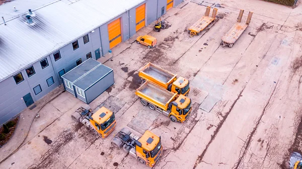 Aerial view over a workshop, factory, recycling facility, warehouse, Outside the building a orange trucks. in front of warehouse. Aerial