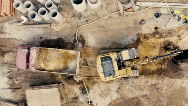 Letecký pohled na bagr sype písek do náklaďáku. Na výstavbu lokality pohled shora. Střelba z dron