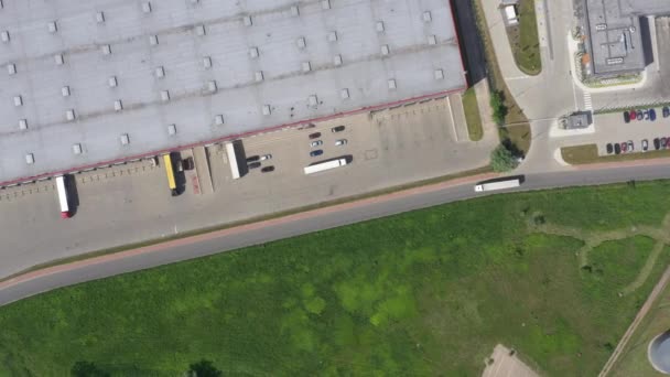 Аэросъемка грузовика с прикрепленным полуприцепом, покидающим промышленный склад / складское помещение / зону погрузки, где загружаются / разгружаются многие грузовики — стоковое видео