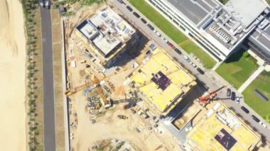 Aerial flight over new constructions site development where heavy machinery and construction workers are working with power tools